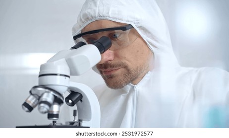 Scientist in ppe analyzing samples with microscope. Close-up of a focused researcher in a lab coat and protective gear using a microscope in a laboratory setting - Powered by Shutterstock