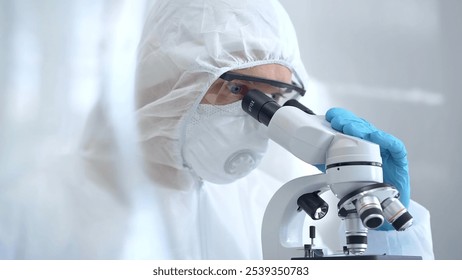 Scientist in ppe analyzing samples using a microscope in a laboratory setting. Close-up of a focused researcher in a lab coat mask and protective gear - Powered by Shutterstock