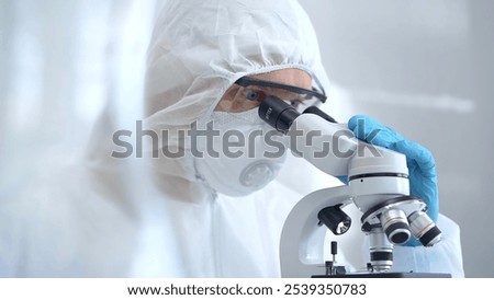 Scientist in ppe analyzing samples using a microscope in a laboratory setting. Close-up of a focused researcher in a lab coat mask and protective gear