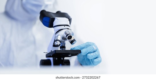 Scientist in protective gear using microscope in laboratory setting, white banner background.
