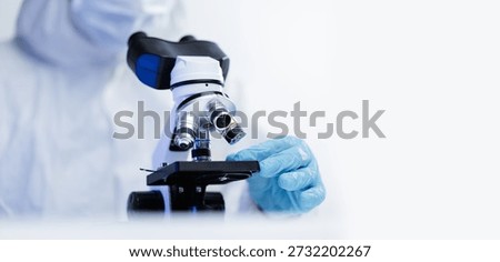 Scientist in protective gear using microscope in laboratory setting, white banner background.