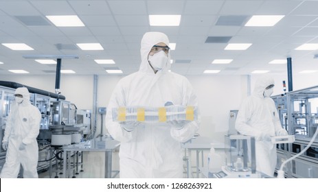 Scientist In Protective Suit Carries Case With Finished Product Through Laboratory. Facility With Modern Industrial Machinery. Product Manufacturing Process: Semiconductors, Biotechnology.