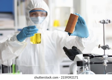Scientist in protective suit holds car filter cartridge in laboratory and oil. Automatic filter check concept