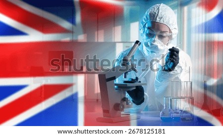 Scientist in protective suit working with microscope and glassware in UK laboratory, medical research, biotechnology, pharmaceuticals, healthcare, science.