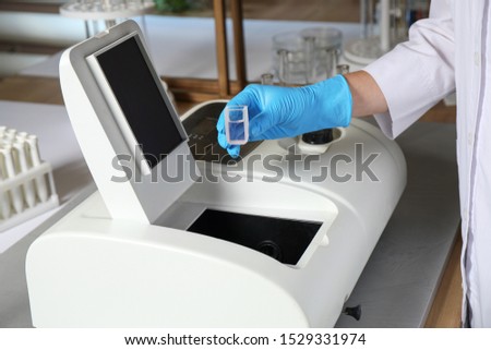 Scientist putting sample compartment with liquid in spectrophotometer, closeup. Laboratory analysis
