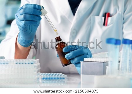 Scientist researcher dosing and mixing fluids in the chemistry lab. Chemist pipetting drop  fluid of a bottle in the product research laboratory