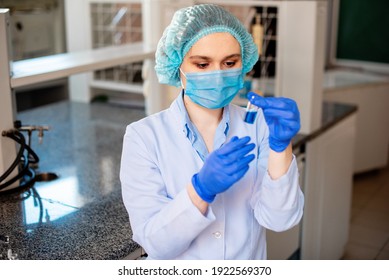 Scientist researching in laboratory. Focused female science professional holding blue solution into the glass cuvette. Healthcare and biotechnology concept.