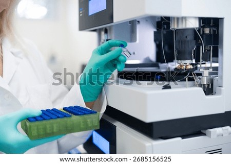 Scientist in rubber gloves carefully loading vial into autosampler for chemical, pharmaceutical, and clinical testing procedures