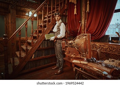 Scientist Steampunk Man Inventor Reads A Book In His Cabinet With Victorian Interior. Adventure World Of Steampunk.