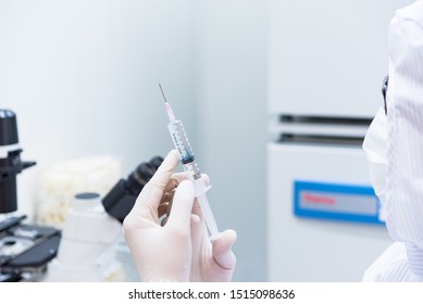 A Scientist In Sterile Coverall Gown Holding A Syringe For Doing Medical Research In Clean Environment. Cleanroom Facility.