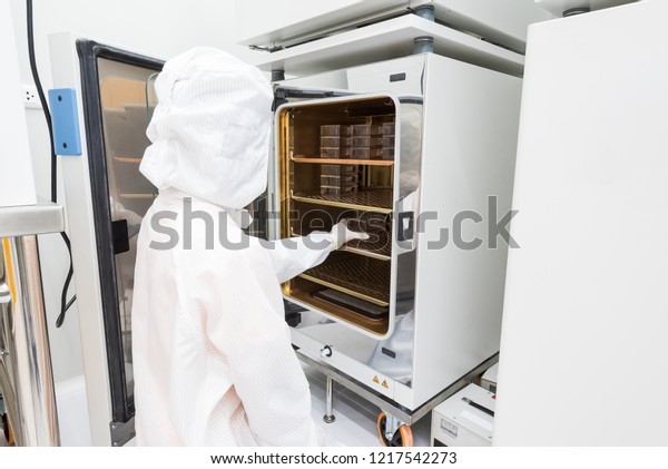 A scientist in sterile coverall gown\
placing cell culture flasks in the CO2 incubator. Doing biological\
research in clean environment. Cleanroom\
facility\
