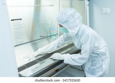 A scientist in sterile coverall gown using alcohol 70% and cleanroom wipes for cleaning Biological safety cabinet(BSC.) in laboratory, before and after using bsc. ,decontamination,Cleanroom facility.