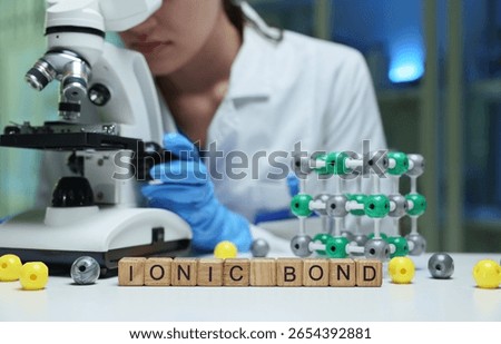 A scientist is studying ionic bonds with a microscope and molecular models in a stateoftheart lab