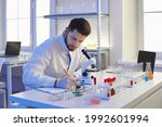 Scientist taking notes on paper. Portrait of serious man in lab coat writing scientific research data analysis report sitting at table with microscope in pharma or microbiology science laboratory