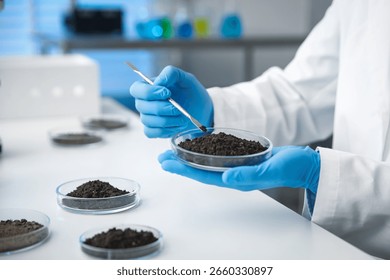 Scientist taking soil sample for research at white table in laboratory, closeup