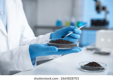 Scientist taking soil sample for research at white table in laboratory, closeup