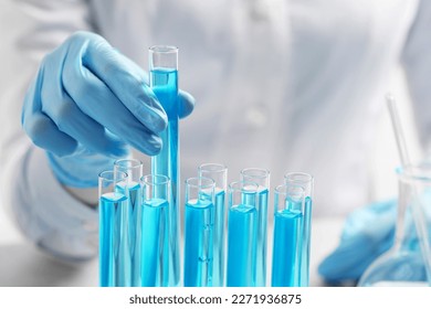 Scientist taking test tube with light blue liquid at table, closeup - Powered by Shutterstock