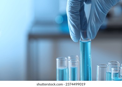 Científico tomando tubo de ensayo con líquido azul claro en laboratorio, cerrando. Espacio para texto