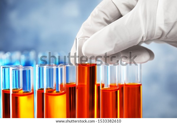 Scientist taking test tube with liquid sample on\
grey background,\
closeup