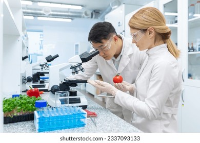 Scientist team asian man and woman testing and researching food, researchers testing vegetables inside laboratory using microscope, workers in white medical coats. - Powered by Shutterstock