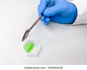 A scientist transferring a portion of green crystals of nickel chloride hexahydrate onto a weighing boat. Nickel chloride is a catalyst used in a variety of industrial processes.