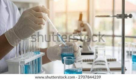 Scientist is using an eyedropper to drop blue liquid into test tubes in the laboratory.