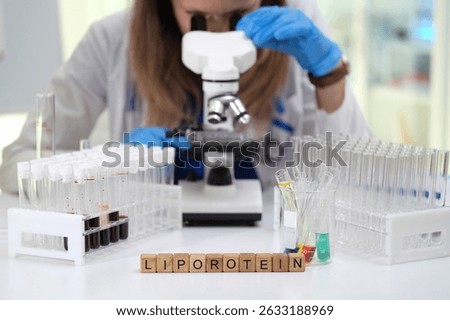 A scientist is using a microscope to conduct detailed lipoprotein research, surrounded by test tubes and samples