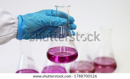 The scientist wear blue nitrile gloves holding Erlenmeyer Conical flask, with purple violet solvent forming reaction boric acid and ammonia solution analysis in wastewater sample. Selective focus.