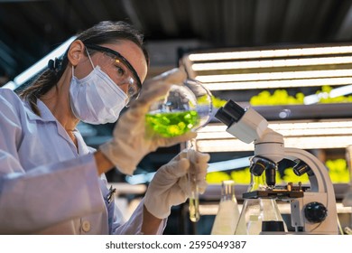 Un científico que lleva una máscara y guantes trabaja en un laboratorio, examinando un líquido verde en un vaso de precipitados y usando un microscopio. La configuración del laboratorio está bien iluminada, lo que refleja un enfoque en investigación, ciencia y experimentación