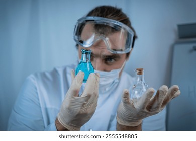 A scientist wearing protective goggles, gloves, and a face mask carefully analyzing vials containing blue and clear liquids, emphasizing precision, research, and scientific inquiry - Powered by Shutterstock