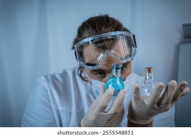 A scientist wearing protective goggles, gloves, and a face mask carefully analyzing vials containing blue and clear liquids, emphasizing precision, research, and scientific inquiry - Powered by Shutterstock