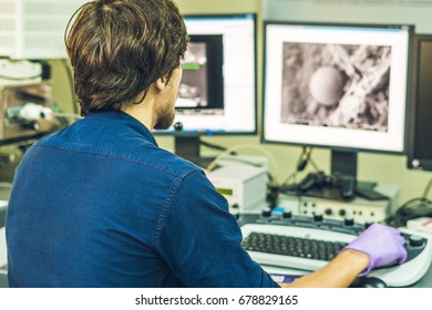 Scientist works at a electron microscope control pannel with two monitors in front of him.
