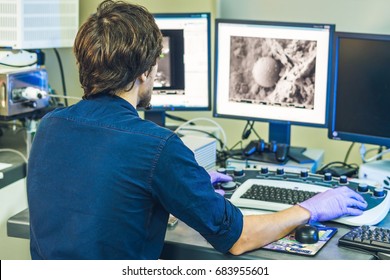 Scientist works at a electron microscope control pannel with two monitors in front of him.