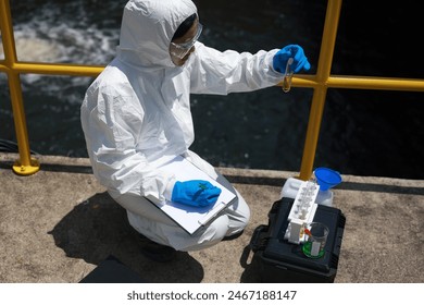 Scientists biologists or researchers in protective suits taking water samples from wastewater from industries. Experts analyze the water in a contaminated environment. - Powered by Shutterstock