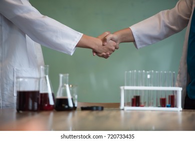 Scientists with business people shake hands with agreement to research and development together in a science pharmacy laboratory.