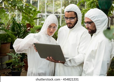 Scientists in clean suit discussing over laptop at greenhouse - Powered by Shutterstock