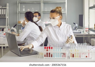 Scientists doing research in well-equipped medical science laboratory. Lab worker or assistant in protective face mask and glasses entering data analysis report in electronic system on laptop computer