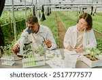 Scientists examining plant samples in modern greenhouse. Scene includes various laboratory equipment and plant specimens while researchers focus on conducting experiments