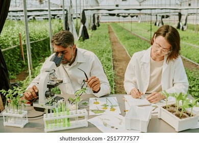 Scientists examining plant samples in modern greenhouse. Scene includes various laboratory equipment and plant specimens while researchers focus on conducting experiments - Powered by Shutterstock