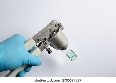 scientist's hand using a manual vial crimper tool to seal an aluminum cap onto a glass autosampler vial containing a green liquid sample. A step in sample preparation for gas chromatography (GC).