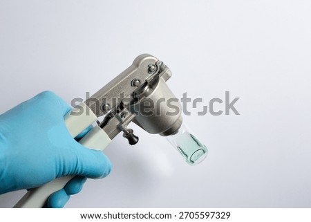 scientist's hand using a manual vial crimper tool to seal an aluminum cap onto a glass autosampler vial containing a green liquid sample. A step in sample preparation for gas chromatography (GC).