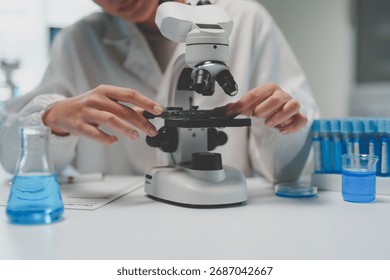 Scientist's hands adjusting a microscope slide for research with blue liquids in beakers and test tubes in a laboratory