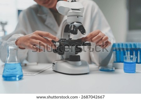 Scientist's hands adjusting a microscope slide for research with blue liquids in beakers and test tubes in a laboratory