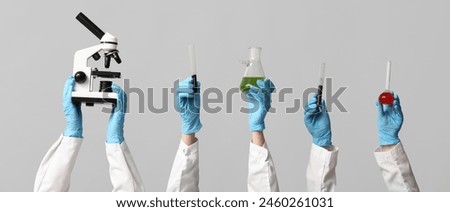 Scientist's hands holding microscope, test tubes with soil and liquids on grey background