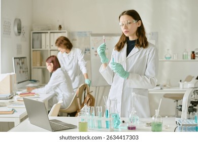 Scientists in lab coats conducting experiments with various chemical substances in modern laboratory environment having lab equipment and devices on benches
