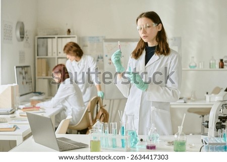 Scientists in lab coats conducting experiments with various chemical substances in modern laboratory environment having lab equipment and devices on benches