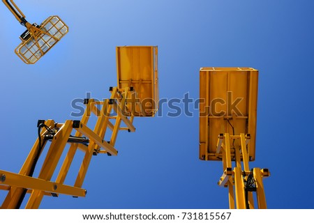 Scissor lift platform, cherry picker, aerial platform with bucket, three yellow construction machines and cranes, heavy industry, blue sky on background, bottom view 