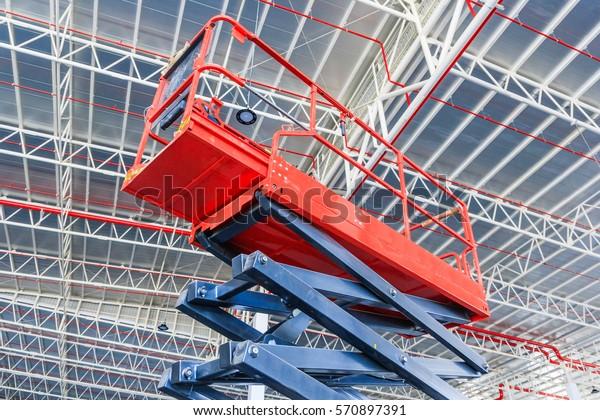 Scissor lift platform with hydraulic system\
elevated towards a factory roof with construction workers, Mobile\
aerial work platform