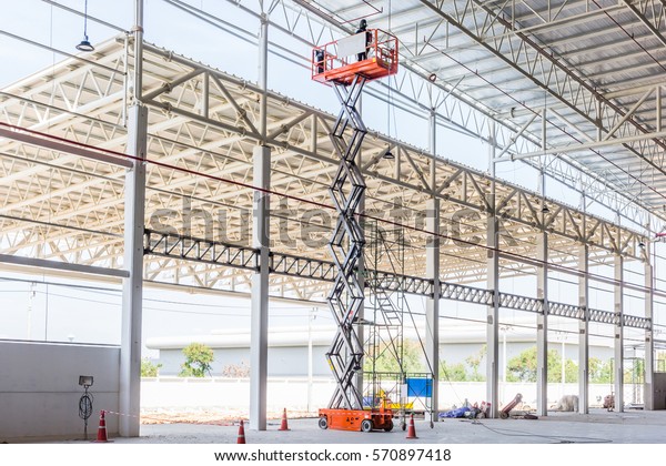 Scissor lift platform with hydraulic system\
elevated towards a factory roof with construction workers, Mobile\
aerial work platform