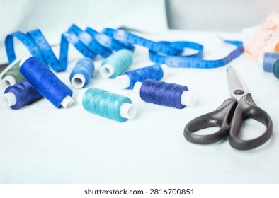 Scissors and blue thread spools on white surface, sewing, tools,